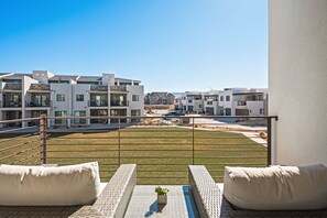 A balcony with a view of modern buildings, a grassy area, and a parking lot.