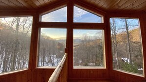 Una cabana amb teulada inclinada i grans finestres que donen vista a un paisatge forestal.