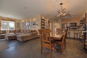 A spacious living area with a large sectional sofa, a dining table with chairs, a kitchen with modern appliances, and a chandelier. - 3 BR 2 BA Ski-in & Ski-out, 50 steps to ski run, unbelievable location! (Mammoth Lakes)