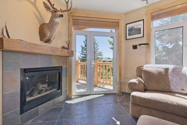A living room with a fireplace, a deer head mounted on the wall, a sofa, and a sliding glass door leading to an outdoor deck. - 3 BR 2 BA Ski-in & Ski-out, 50 steps to ski run, unbelievable location! (Mammoth Lakes)