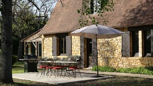 Ein Steinhaus mit Terrasse, Sitzgelegenheiten im Freien und einem Grill.