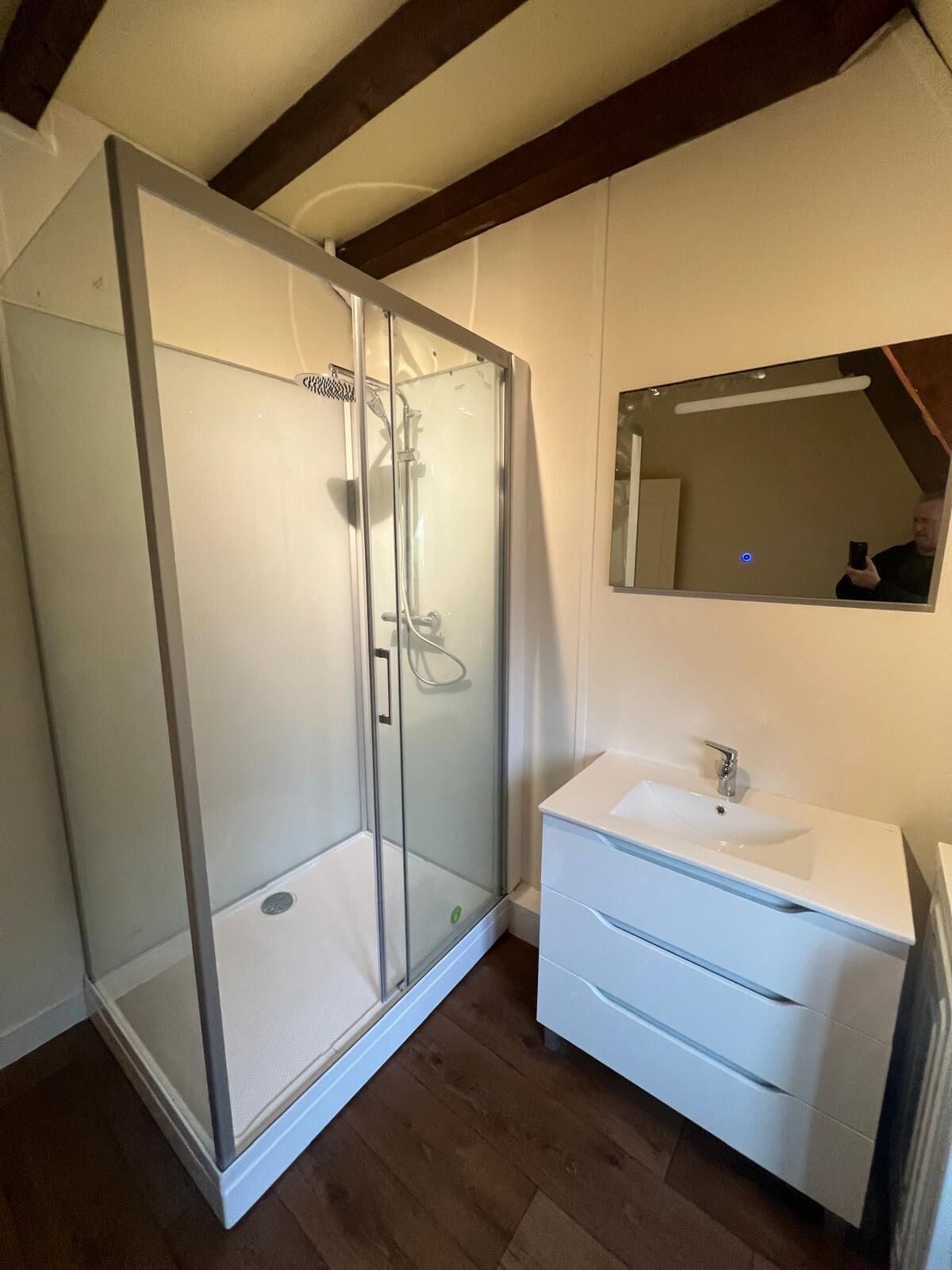 Une salle de bain moderne avec une douche à parois de verre, un lavabo blanc et un miroir au-dessus.