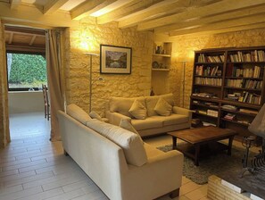 Relax in this inviting living room with a sofa, armchair, and floor lamp, surrounded by a book collection and a large window.
