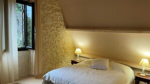Ein Schlafzimmer mit einem großen Bett, zwei Nachttischlampen, einer Steinwand und einem Fenster.