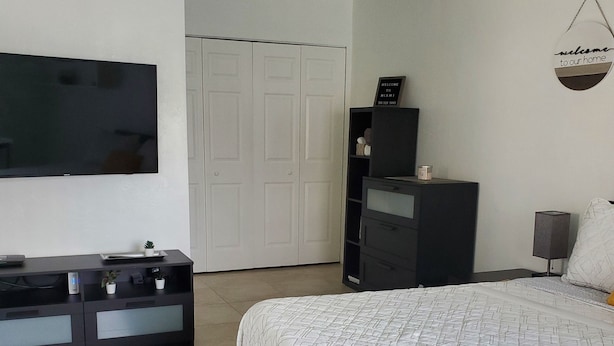 A bedroom with a bed, a TV mounted on the wall, a wardrobe, and a door in the background. -  Cozy suite with private entrance and parking! (Miami)