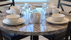 A round dining table with white ceramic cups and saucers, black chairs, and a window with blinds in the background. - SC (3745) 2BDR Townhouse Ft Jackson.   (Columbia)