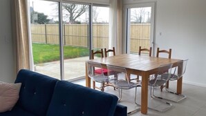 A modern living room with a blue sofa, a wooden dining table with chairs, and large sliding glass doors leading to a backyard. - New house by the sea, Plounéour Brignogan Plages  (Plounéour-Brignogan-plages)