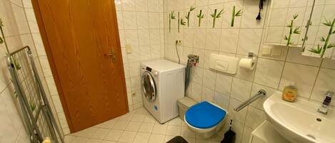 A compact bathroom with a washing machine, toilet, sink, and a shower area.