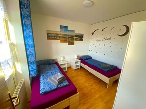 Un dormitorio con dos camas individuales, una mesita de noche, una obra de arte en la pared y una lámpara en el techo.