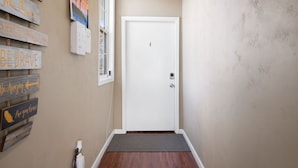 A hallway with a white door, wooden signs with motivational phrases, a small rug, and a wall-mounted thermostat. - Cozy 1bdr/1br near downtown (Sacramento)