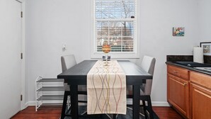 A dining area with a table set for two, a window with blinds, and a kitchen area with wooden cabinets. - Cozy 1bdr/1br near downtown (Sacramento)