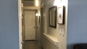 Um corredor com uma porta, um espelho fixado na parede e um acessório de iluminação.