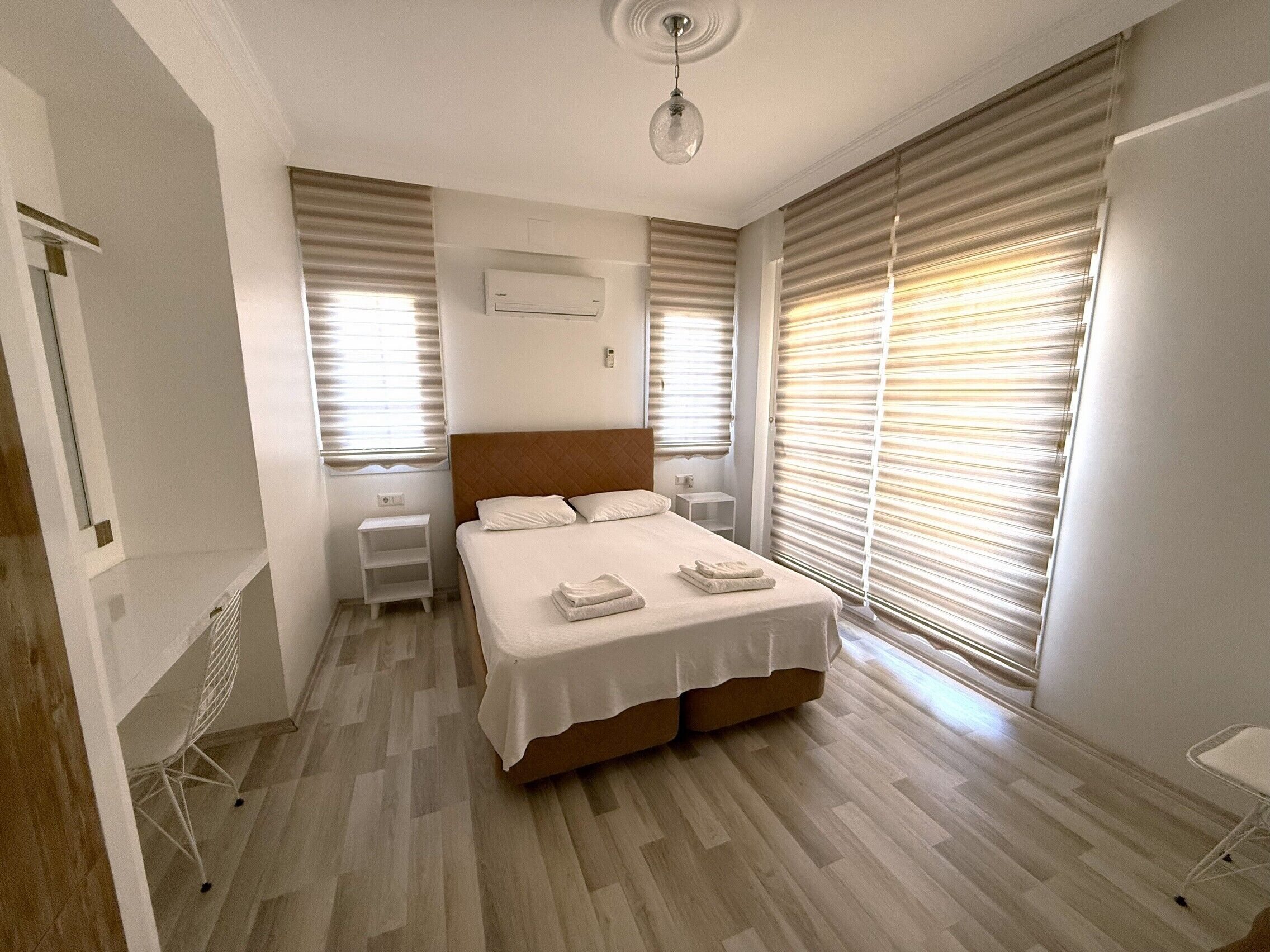 Une chambre à coucher comprenant un lit, des tables de chevet, un appareil de climatisation et de grandes fenêtres équipées de stores.