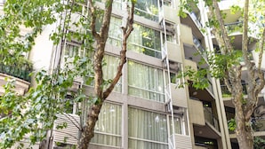 Un immeuble à plusieurs étages, doté de balcons, de grandes fenêtres et d’un arbre devant.