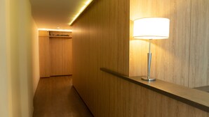 Un couloir aux murs recouverts de lambris en bois, agrémenté d’un lampadaire au design moderne et d’un spot encastré au plafond.