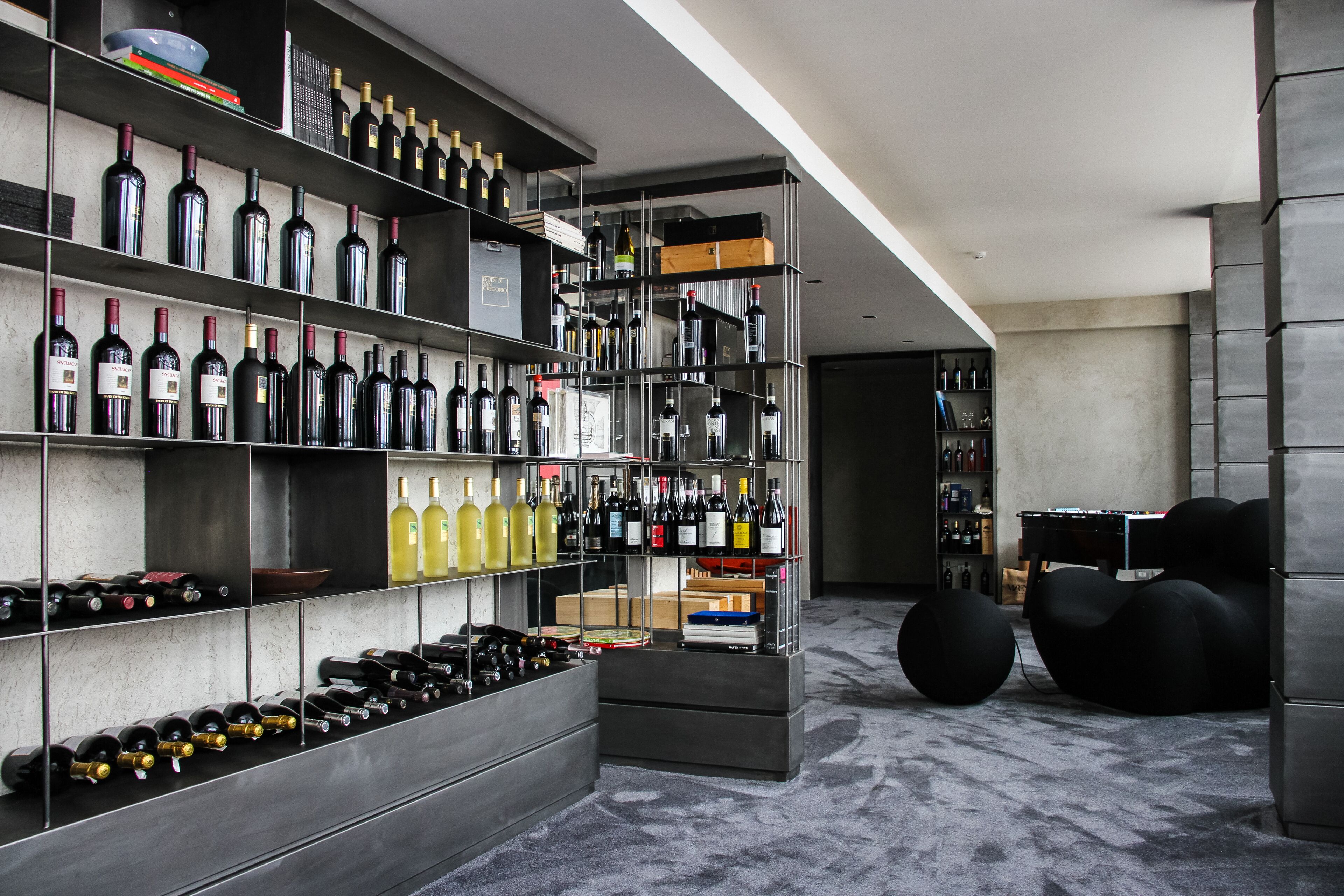 A modern wine cellar with multiple shelves of wine bottles, a seating area, and a cozy atmosphere.
