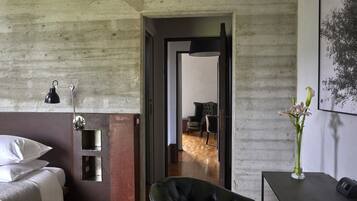 Habitación de hotel con cama, una silla, escritorio con un florero y una puerta que da a otra habitación.