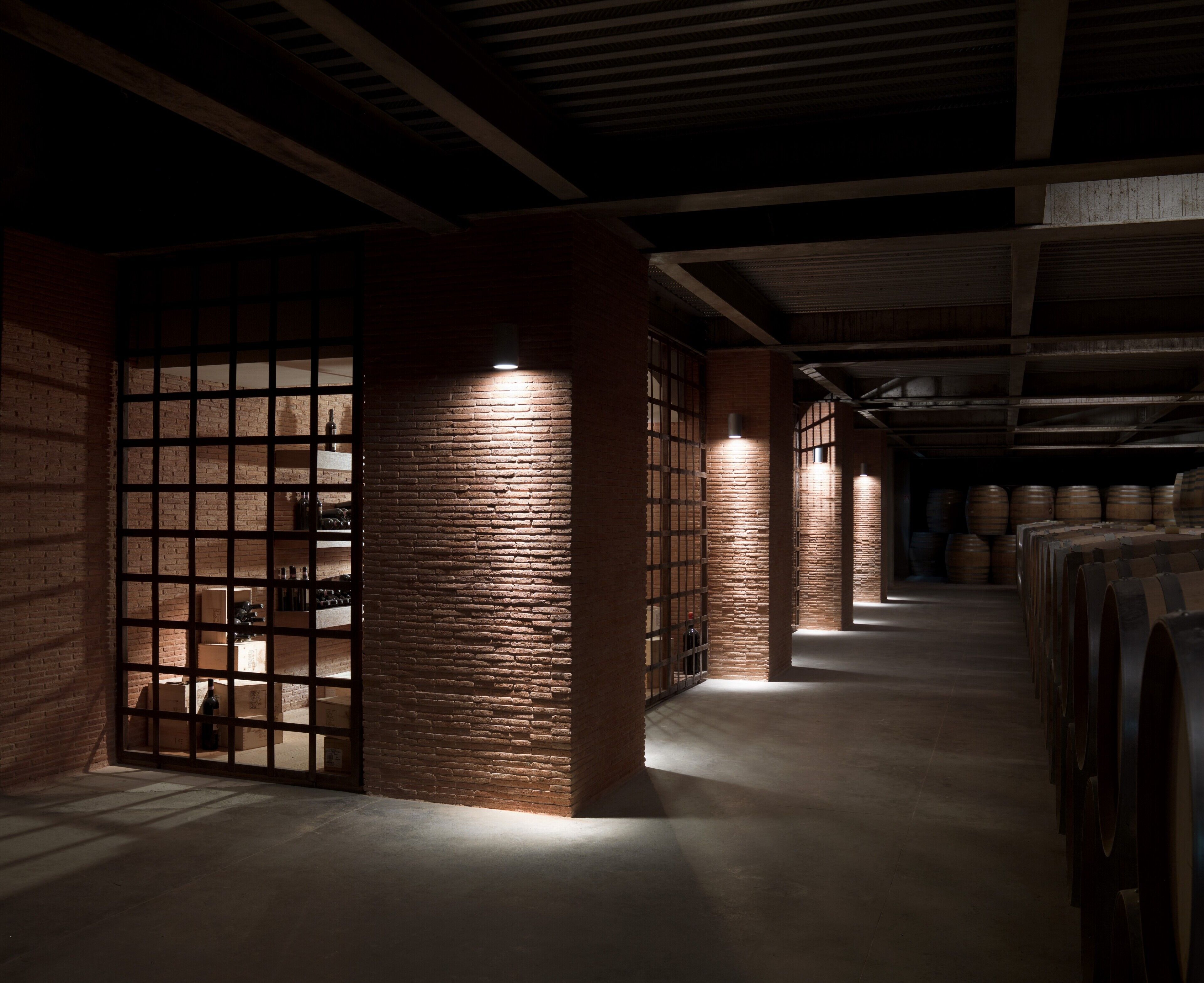 Un interior estilo almacén, tenuemente iluminado, con paredes de ladrillo, vigas de madera y barriles.