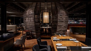 Um restaurante moderno com área de jantar central, um bar com diversos tipos de garrafas e disposição de mesas e cadeiras.