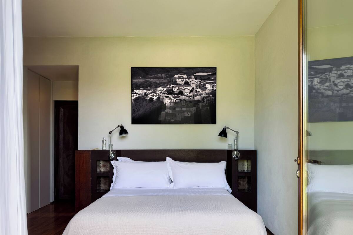 A hotel room with a large bed, two bedside lamps, a framed black and white photograph on the wall, and a wooden floor.