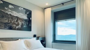 Quarto de hotel com uma cama grande, um quadro na parede, uma mesa de cabeceira e uma janela com vista para o mar.