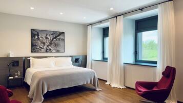 A modern bedroom with a large bed, a nightstand, a red chair, and a window with curtains.