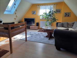 Ein gemütliches Wohnzimmer mit einem Holzstuhl, einer Couch, einem Fernseher und einer Pflanze.