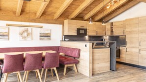 A modern kitchen with wooden cabinets, a built-in island, and a seating area with chairs. - Superior Chalet # 4C with sauna (Uttendorf)