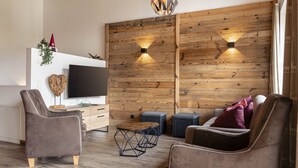A modern living room with a wooden accent wall, a flat-screen TV, two armchairs, a coffee table, and a side table. - Superior Chalet # 4C with sauna (Uttendorf)