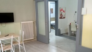 Ett modernt hotellrum med ett träbord, ett vitt skrivbord och en stol. På väggen sitter en tv, det finns ett element och en dörr som leder till ett annat rum.