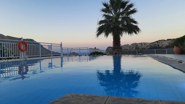 A swimming pool with a lifebuoy, palm tree, and rocky hills in the background. - About Villa Selene (Archangelos)