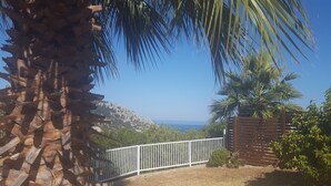A coastal view with a white fence, palm trees, and a rocky hill in the background. - About Villa Selene (Archangelos)
