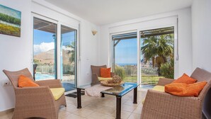 A balcony with wicker furniture, a glass table, and a view of the sea and hills. - About Villa Selene (Archangelos)
