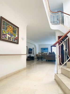 A spacious living area with a high ceiling, a staircase with a white railing, and a painting on the wall.