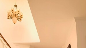 Un pasillo espacioso con una puerta doble de madera, una escalera con barandilla y un candelabro.