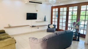 Una sala de estar con un sofá gris, un televisor montado en la pared y un ventanal con vistas a zonas verdes.