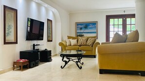 Una sala de estar con un sofá, una mesa de centro, un televisor y obras de arte enmarcadas en las paredes.