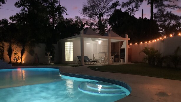 Una piscina de borde curvo, un área de terraza techada con sillones y luces colgantes.