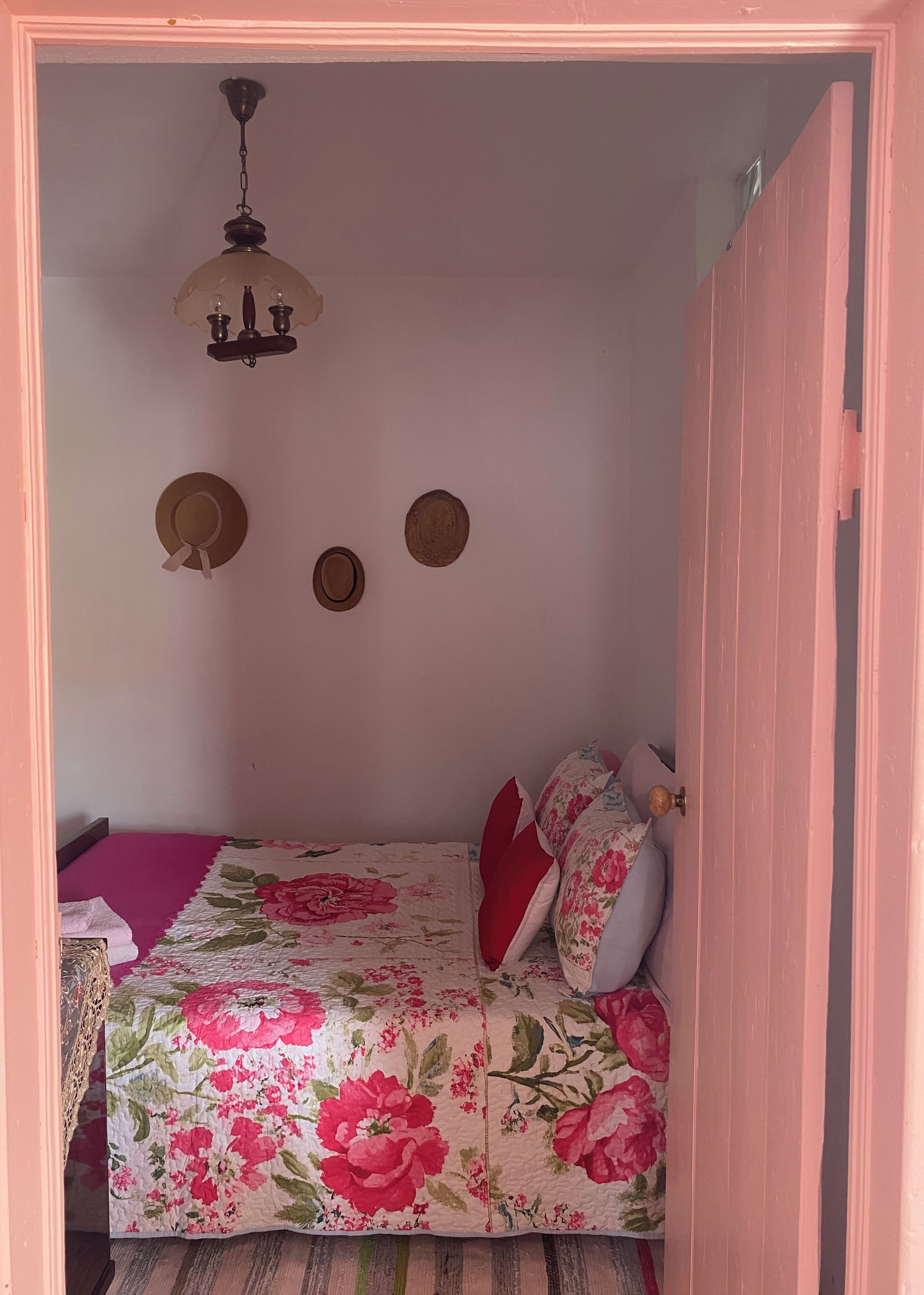 Un dormitorio con colcha estampada, ventilador de techo y puerta con marco rosa.