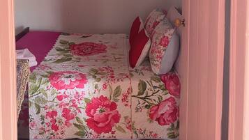 Un dormitorio con colcha estampada, ventilador de techo y puerta con marco rosa.
