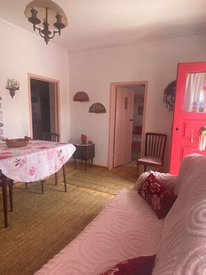 A dining area with a table covered in a floral tablecloth, a chandelier, and a red door. - CASAL DOS CARPINTEIROS 1 - Beach and Countryside (Silveira)