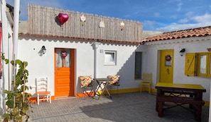 A white building with a tiled roof, a wooden fence, a table, chairs, and a bench. - CASAL DOS CARPINTEIROS 1 - Beach and Countryside (Silveira)