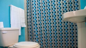 A bathroom with a toilet, a blue towel, and a patterned shower curtain.