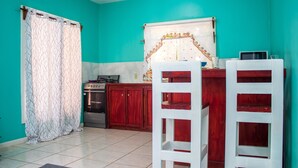 A kitchen with teal walls, a stove, and wooden cabinets. There are two white chairs and a microwave on the counter.