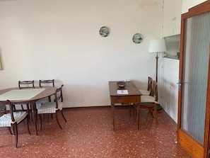 A dining area with a wooden table and chairs, a small table with a bowl and a piece of paper, and a lamp.