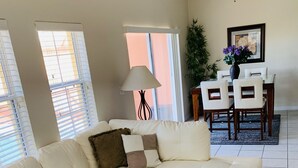 A living room with a sectional sofa, a coffee table, a dining table with chairs, a lamp, and a potted plant. - Only 5 minutes from Walt Disney World (Kissimmee)