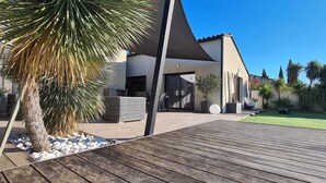 A modern house with a wooden deck, a palm tree, and a well-maintained lawn. - Villa with pool in a haven of peace (Sommières)