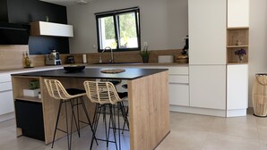 A modern kitchen with a central island, two bar stools, a window, and built-in appliances. - Villa with pool in a haven of peace (Sommières)