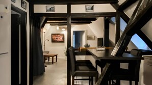 A dining area with a high ceiling and exposed beams, a table with chairs, and a view through an open door.