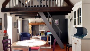 Een gezellige kamer met een houten trap, een ronde tafel met stoelen, een boekenkast en een bed met een blauwe stippen hoes.
